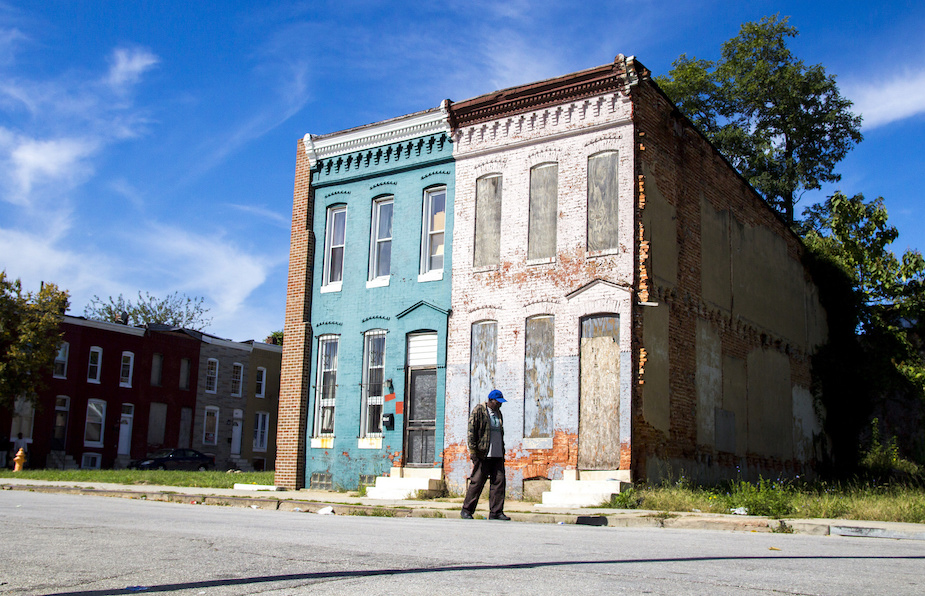 A man walks past two rowhouses in Baltimore's Sandtown-Winchester neighborhood. Elena Iwata / Flickr
